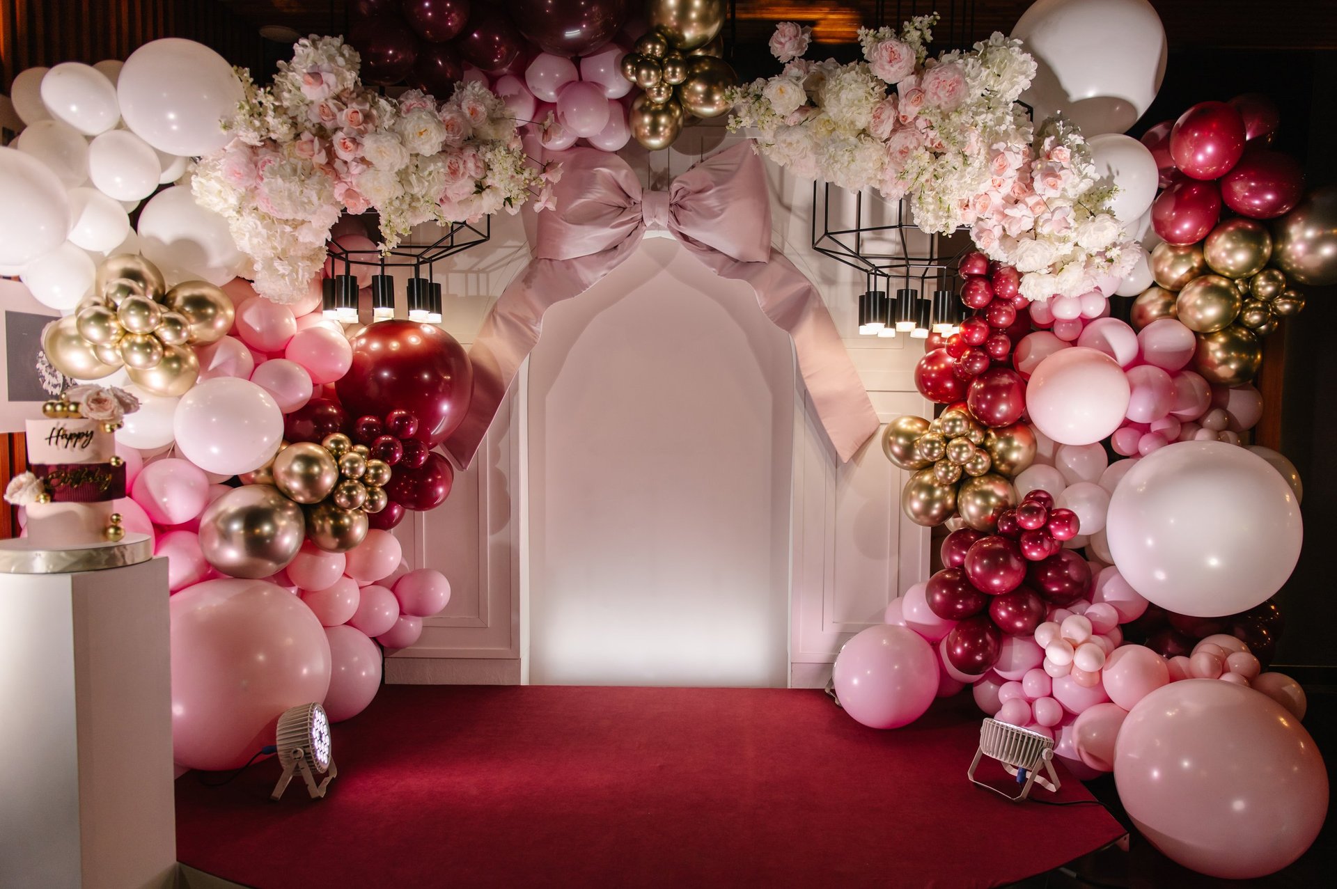 Birthday party decorations with pink roses, Happy Birthday text topper, and gold decor on background of balloons