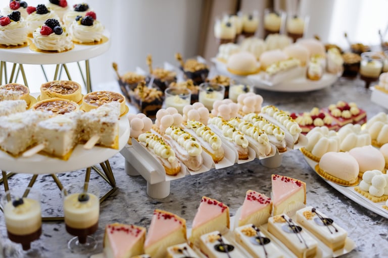 Όμορφη ποικιλία από λεπτά γλυκά, όπως cupcakes, μακαρόν και εκλέρ, κομψά τοποθετημένα σε λευκή πολυώροφη βάση για candy bar
